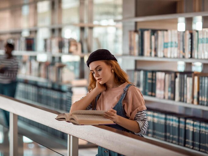 Frau liest Buch in einer Bibliothek | © Getty Images/Marko Geber