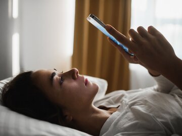 Person liegt im Bett und schaut auf Handy. | © Getty Images/Oleg Breslavtsev