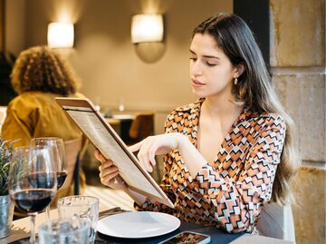 Person sitzt an Restauranttisch mit Menükarte | © Getty Images/Jordi Salas