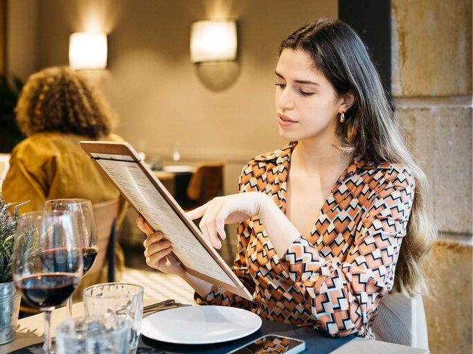 Person sitzt an Restauranttisch mit Menükarte | © Getty Images/Jordi Salas