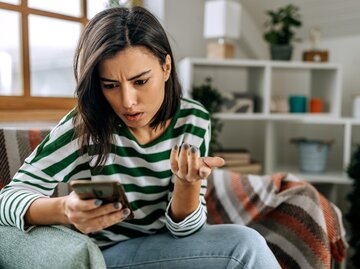 Eine junge Frau schaut besorgt und verärgert auf ihr Handy | © GettyImages/Pekic