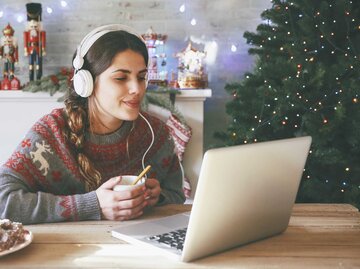 Frau sitzt zu Weihnachten mit Kopfhörern am Laptop. | © Getty Images/Westend61