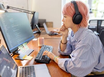 Person sitzt am PC mit Kopfhörern | © Getty Images/Luis Alvarez