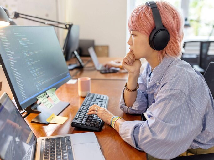 Person sitzt am PC mit Kopfhörern | © Getty Images/Luis Alvarez