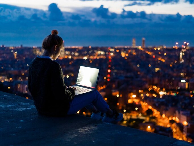 Frau sitzt mit Laptop über beleuchteter Stadt | © gettyimages.de | Westend61