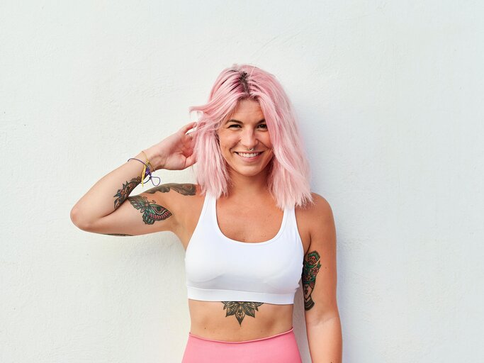 Frau mit rosa Haaren und Tattoos posiert in Sportklamotten | © Getty Images/F.J. Jimenez