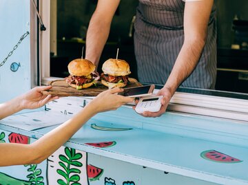 Nahaufnahme, wie eine Person kontaktlos bezahlt und zwei Burger entgegennimmt | © Getty Image/	VioletaStoimenova