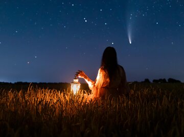 Frau hat Laterne in der Hand und schaut in den Nachthimmel | © Getty Images/Anton Petrus