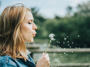 Frau pustet an Löwenzahn | © Getty Images/Dariusz Makowski / EyeEm