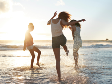 Drei Frauen springen durchs Meer am Strand | © Getty Images/Klaus Vedfelt
