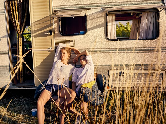 2 Frauen sitzen vor Wohnmobil in der Sonne | © Getty Images/Oliver Rossi