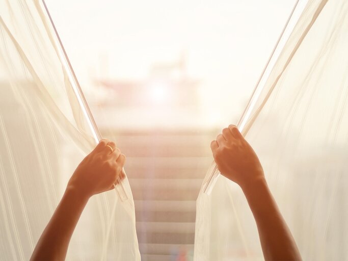 Hände ziehen die Gardinen am Fenster zu | © Getty Images/Prasert Krainukul