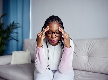 Frau sitzt erschöpft auf der Couch und fasst sich an den Kopf | © Getty Images/Ekaterina Goncharova