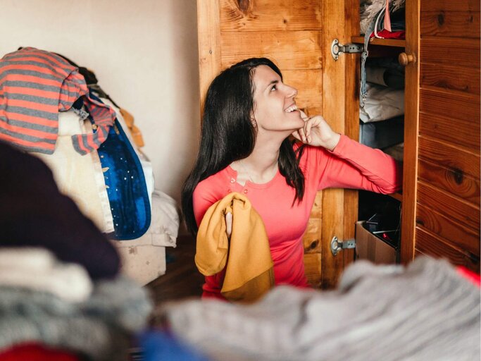 Frau sitzt vor Kleiderschrank und mistet aus. | © Getty Images/urbazon