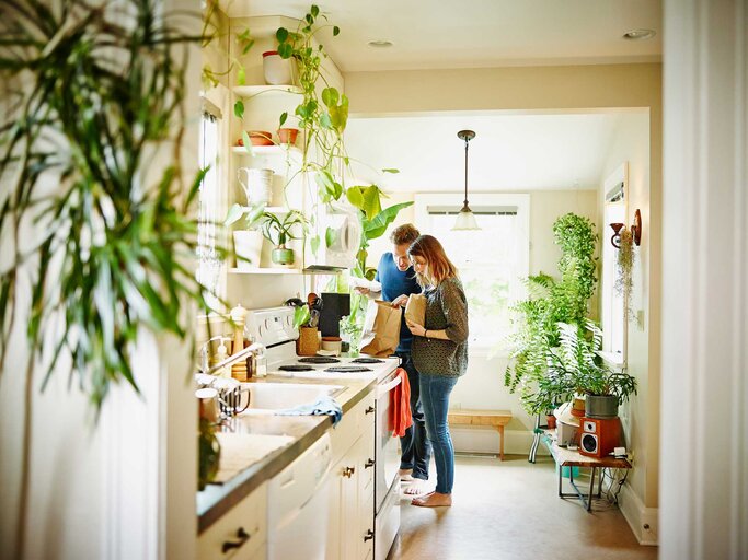 Junges Paar steht in der Küche voller Pflanzen. | © Getty Images / Thomas Barwick