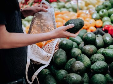 Frau hält im Supermarkt eine Avocado in der Hand.  | © Getty Images / d3sign