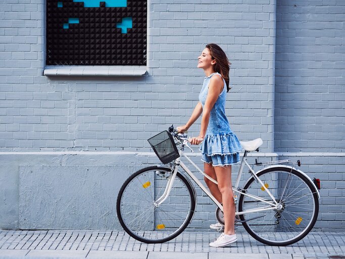 Lachende Frau in einem Jeanskleid auf dem Fahrrad | © Getty Images/BartekSzewczyk