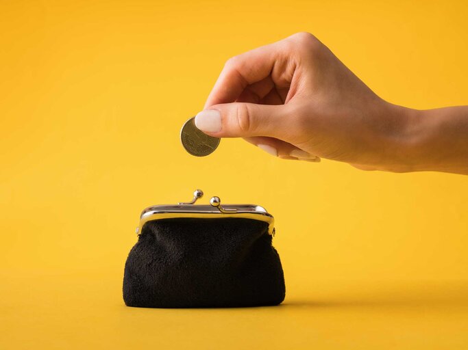 Hand wirft Münze in Geldbeutel | © Getty Images/busracavus