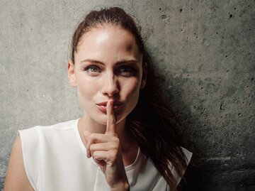Junge Frau mit Finger auf Lippen vor einer Wand | © Getty Images/Portra