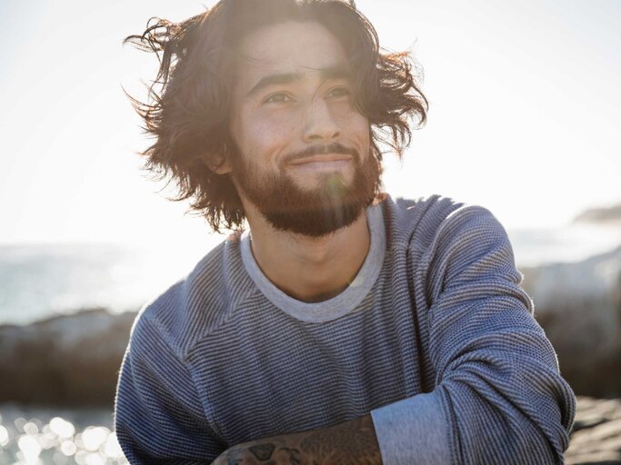 Mann mit langen Haaren in der Sonne am Strand | © Getty Images/The Good Brigade