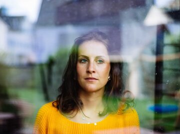 Frau mit gelbem Shirt blickt aus dem Fenster | © Getty Images/Matthias Lindner