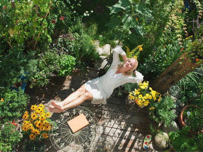 Frau liegt in einem Liegestuhl in ihrem Garten | © Getty Images/Hans Huber