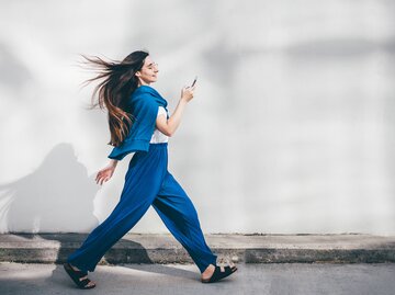 Eine junge Frau geht rasant und schaut auf ihr Handy | © GettyImages/Maria Korneeva