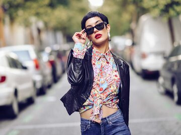 Junge Frau trägt auf der Straße eine Lederjacke und Sonnenbrille und ist sehr selbstbewusst. | © Getty Images / Westend61