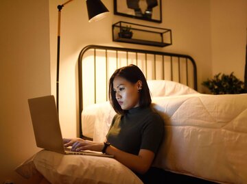 Person sitzt vor Bett am Boden mit Laptop | © Getty Images/Carlina Teteris