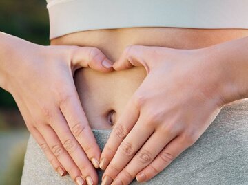 Person formt mit Händen Herz um Bauchnabel | © Getty Images/PeopleImages