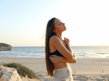 Frau am Strand umarmt sich selbst | © Getty Images/Westend61