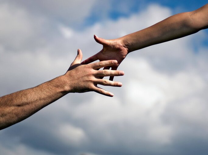 Zwei Hände, die nach einander greifen. | © Getty Images/Andy Andrews