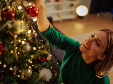 Frau schmückt glücklich einen Weihnachtsbaum. | © Adobe Stock/bernardbodo