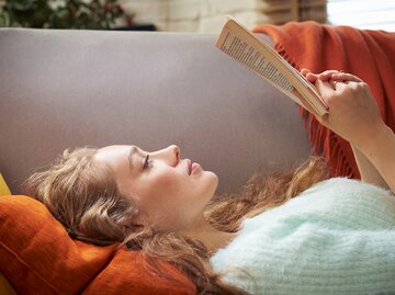 Frau liegt auf dem Sofa und liest | © GettyImages/Tara Moore