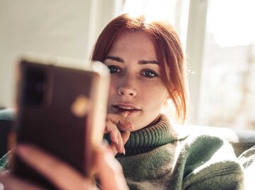 Rothaarige Frau schaut gebannt auf ihr Mobiltelefon | © Getty Images/Guido Mieth