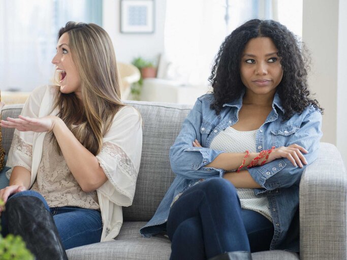Zwei Frauen unterhalten sich, während eine dritte Frau mürrisch guckt | © Getty Images/JGI/Jamie Grill