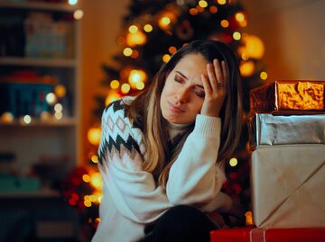 Frau sitzt vor einem Weihnachtsbaum und hält ich gestresst den Kopf. | © Adobe Stock/nicoletaionescu