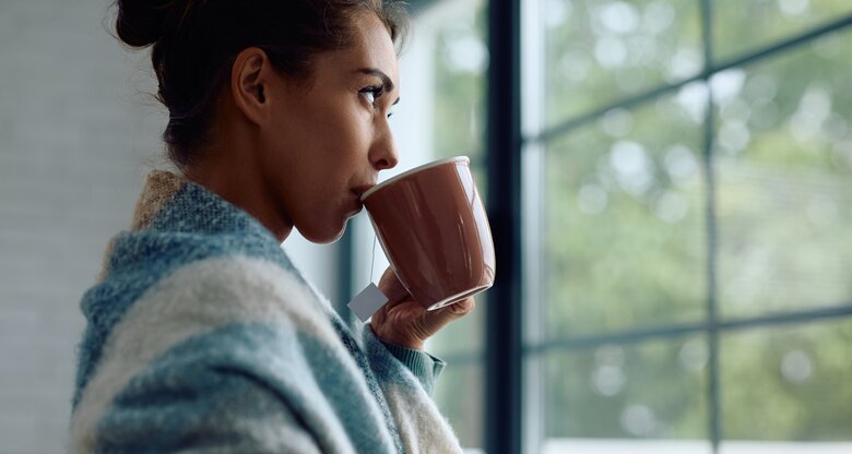 Frau steht am Fenster und trinkt Tee | © AdobeStock/Drazen