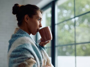 Frau steht am Fenster und trinkt Tee | © AdobeStock/Drazen