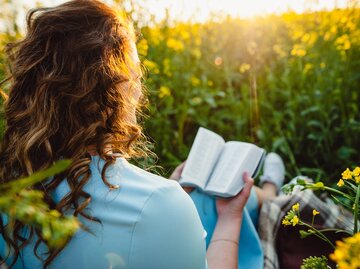 Frau sitzt auf Feld mit Blumen und liest Buch | © shutterstock/Oleksandr Yakoniuk