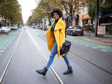 Frau in gelbem Mantel geht über die Straße | © Getty Images/Luis Alvarez