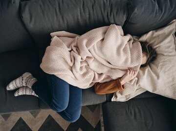 Frau unter der Wolldecke auf Couch | © Getty Images/Anna Bizon/EyeEm