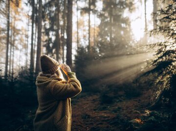Frau steht in Sonnenstrahlen im Wald | © Getty Images/Liliya Krueger