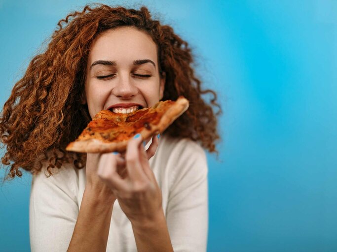 Frau beißt in ein Stück Pizza | © Getty Images/StefaNikolic