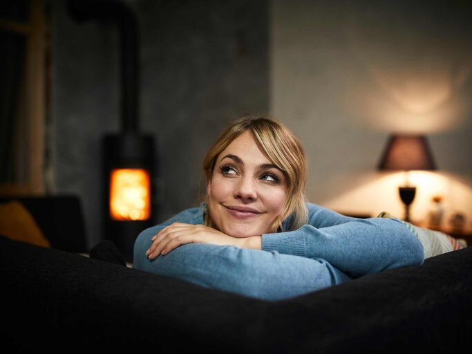 Frau sitzt gemütlich lächelnd auf dem Sofa | © Getty Images/Westend61