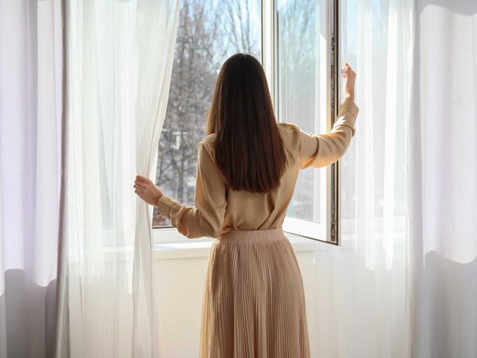 Frau steht am offenen Fenster | © Adobe Stock/Pixel-Shot