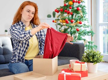 Frau packt unzufrieden eine Weihnachtsgeschenk aus | © Adobe Stock/Paolese