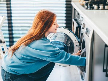 Junge Frau gefüllt die Waschmaschine | © Getty Images/Maria Korneeva