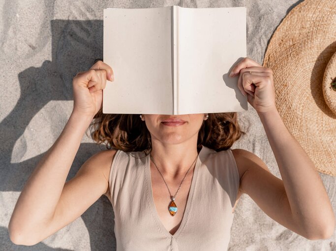 Frau mit Buch am Strand | © Getty Images/Carlos Pintau