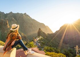 Frau mit Sonnenhut vor Aussicht auf Berge und Sonnenuntergang